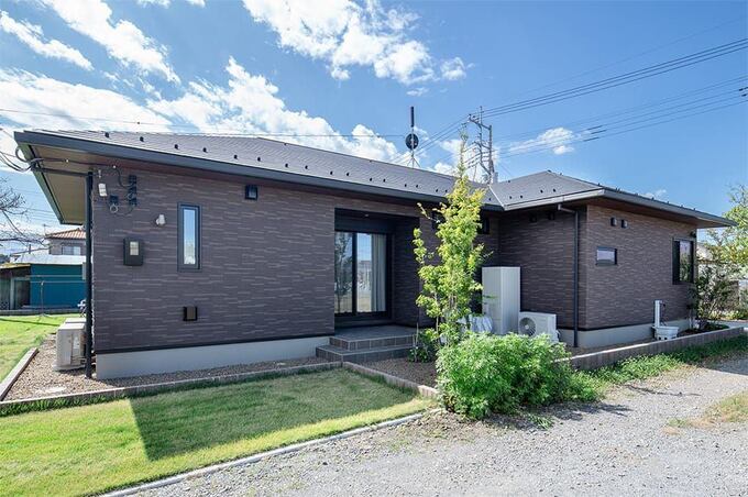 ブラウンの外壁と緑のコントラストが美しい平屋住宅の外観。落ち着いたデザインが周囲の風景に調和している。
