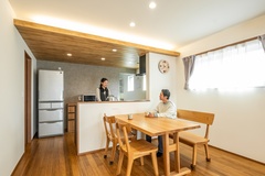 木の温もりに包まれたダイニングで、ご夫婦が楽しそうに会話するひととき。家族の時間を心地よく育む、柔らかな光が魅力です。【イデキョウホーム】