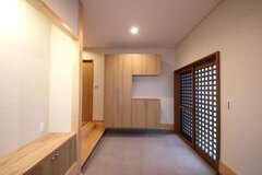 木製の収納と扉が調和した玄関ホール。広々として木目調の温かみある空間は、初めて訪れた人も優しく迎え入れるような雰囲気を感じさせます。【アキヤマ】