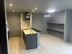モダンなデザインのLDKスペース。キッチンは落ち着いた配色で、対面式のカウンターが特徴的。壁面の棚が収納を豊富にサポート。【建築システム（狭小住宅専門店）】