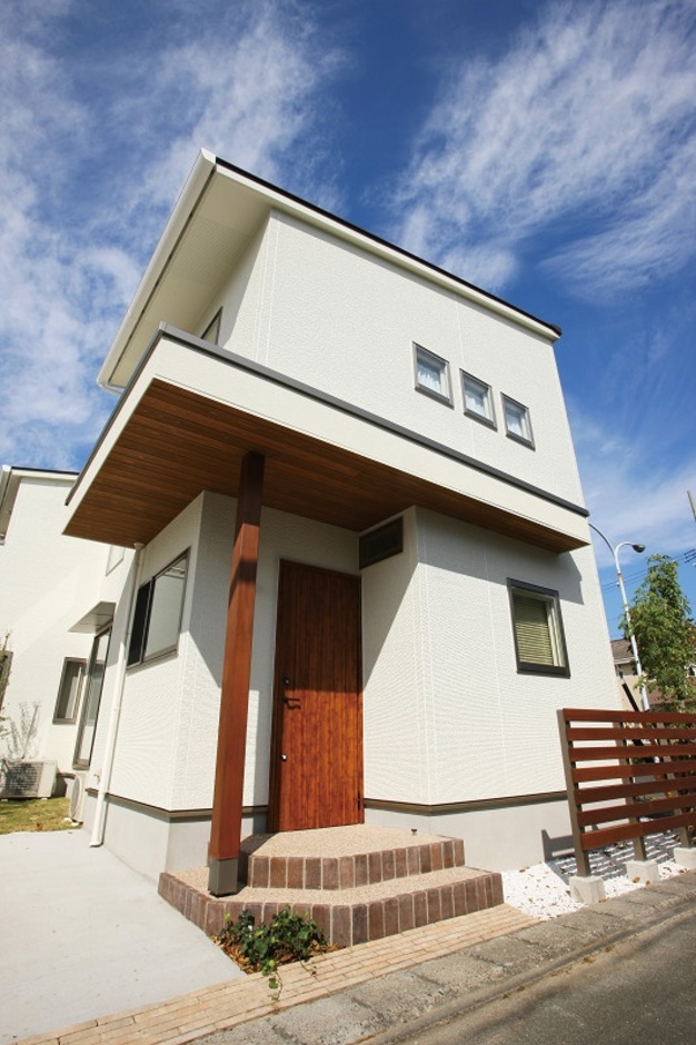 モダンなデザインの二階建て住宅の外観。木製の玄関ドアとベランダがアクセントになっている。【くふうイエタテ】