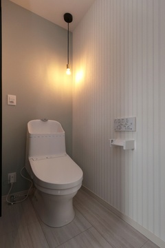 シンプルで落ち着いたデザインのトイレ空間。壁の照明が柔らかな雰囲気を演出し、清潔感と温かみを提供している。