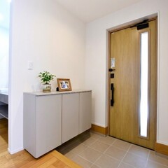 木製ドアとシンプルな収納家具が印象的な玄関。明るい照明で温かみのある空間を演出し、訪れる人を迎える。【木の花ホーム】