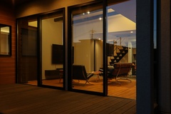 夜の雰囲気を楽しめるテラスから見えるリビングルーム。温かい光がもれるガラス扉が魅力的で、外と室内のつながりを感じさせる。