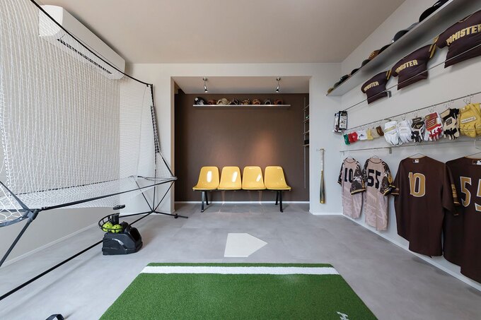 ご主人の夢を叶えた「野球部屋」。素振りができるほどの広さを確保し、グローブやバットをディスプレイできる棚やベンチを備えた空間は、まるで専用スタジアムだ