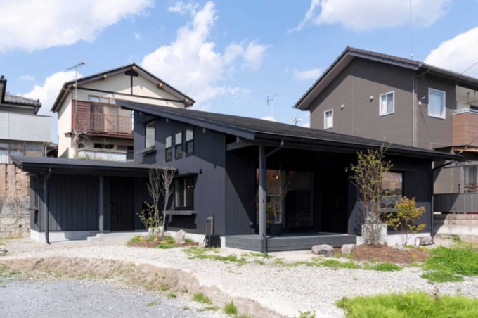 モダンな黒い外壁が特徴的な平屋建築。庭には緑が点在し、落ち着いた住宅街に溶け込んでいる。
