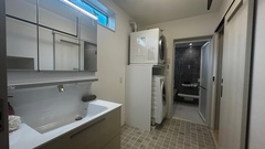 洗面スペースと一体化したランドリールーム。キッチン横のパントリーから通りぬけられ、洗濯機の上に収納スペースも確保し、効率的な家事動線になっている。モダンなデザインで清潔感がある空間。