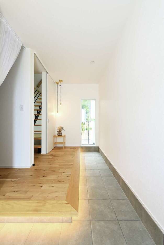玄関に入ると土間が奥まで続き、窓の先には坪庭が見える。視線が外へ抜け、いっそう開放的に。間接照明やペンダント照明も効果的に活かされている