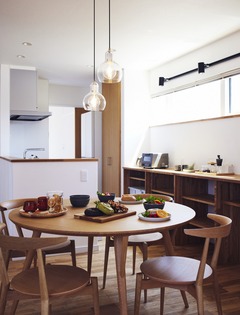 丸テーブルと木製の椅子が温かみを感じさせるダイニング。ペンダントライトが雰囲気を引き立て、窓から光が差し込む明るい空間である。