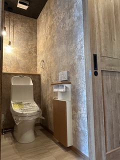 暖かみのある色調で仕上げられたトイレの空間。壁の質感が洗練されており、照明が柔らかく空間を照らしている。