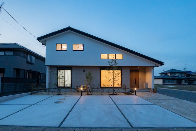 夕暮れ時にライトアップされたモダンな平屋建物の外観。広々とした駐車スペースがあり、落ち着いた住環境が感じられる。