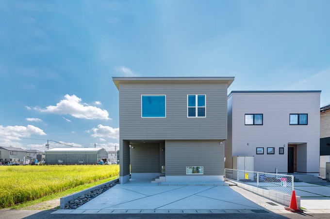 シンプルでモダンなデザインの住宅外観。広々とした前庭と空が広がり、開放感を感じさせるのが特徴である。