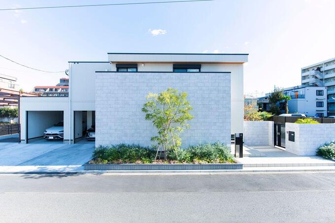 モダンでシンプルな外観の住宅。白い壁と庭の緑が調和し、落ち着いた印象を与えるデザイン。