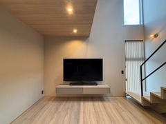 シンプルでモダンなリビング空間。壁掛けのテレビが際立ち、天井のスポットライトが余裕のある明るさを提供している。【E-HOME（イーホーム）】